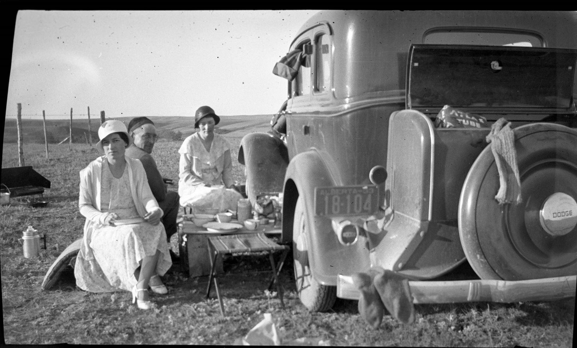 Group sitting near car having picnic